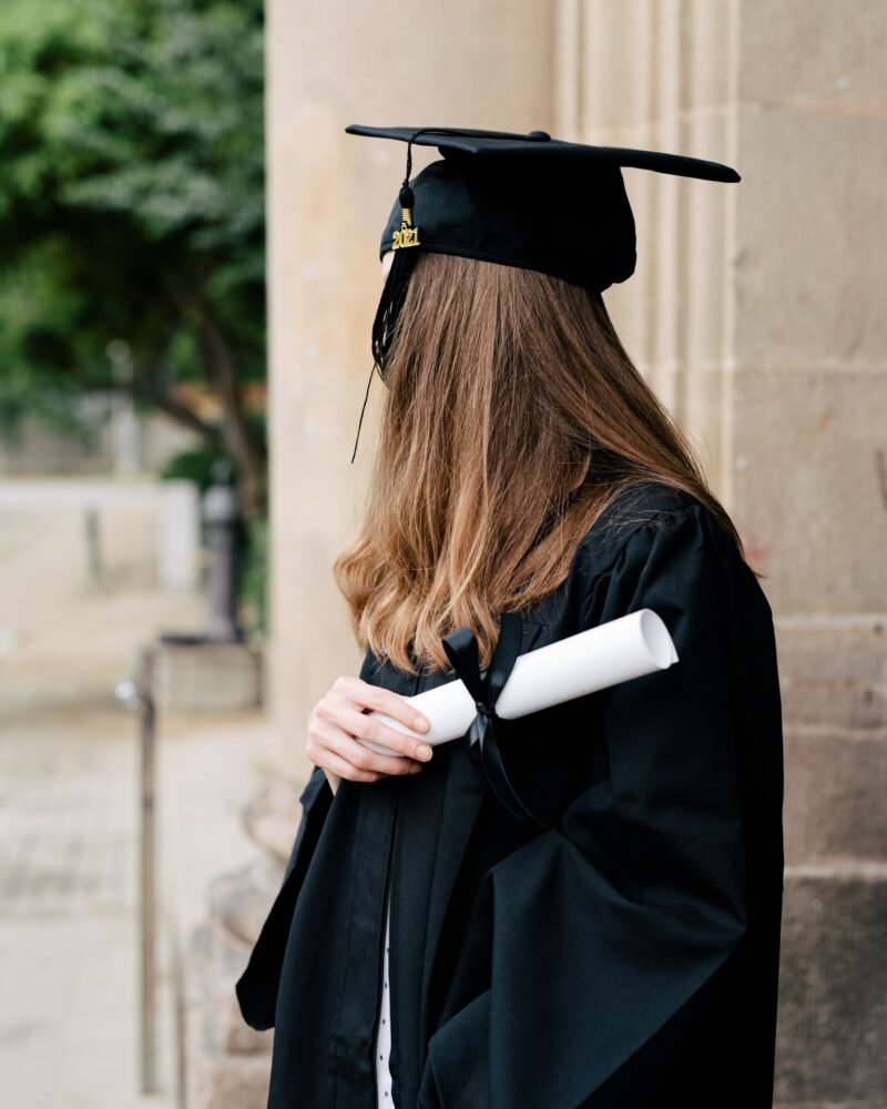 A university graduate in cap and gown holding a rolled diploma.