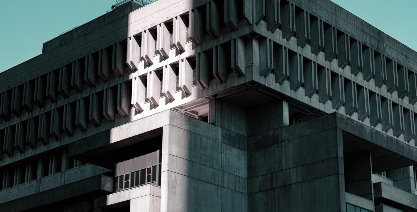 A brutalist concrete office building against a teal sky