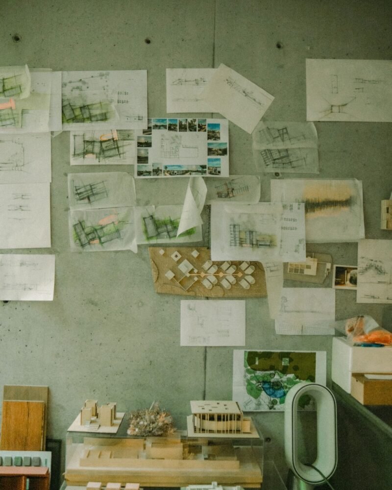 Architectural sketches and models pinned to a concrete studio wall
