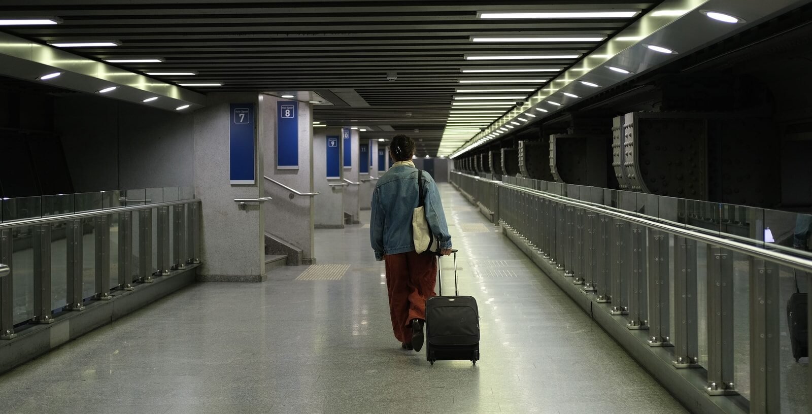 A traveller with a suitcase walking down a long, brightly lit concourse
