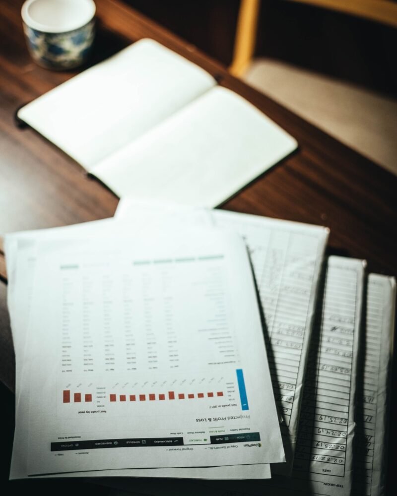 Printed financial reports and an open notebook spread across a wooden desk