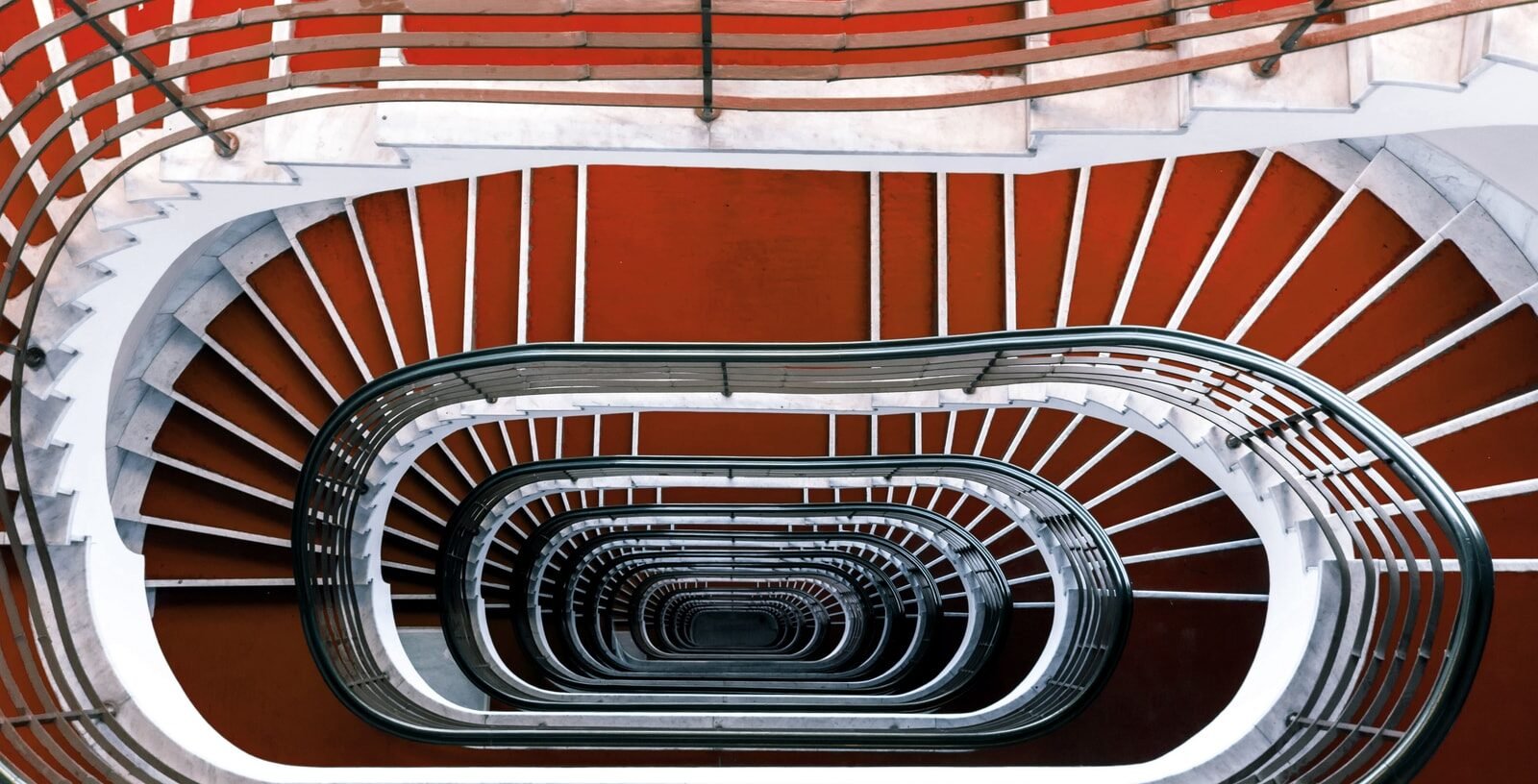 Looking down a red and white spiral staircase with a dark curved handrail