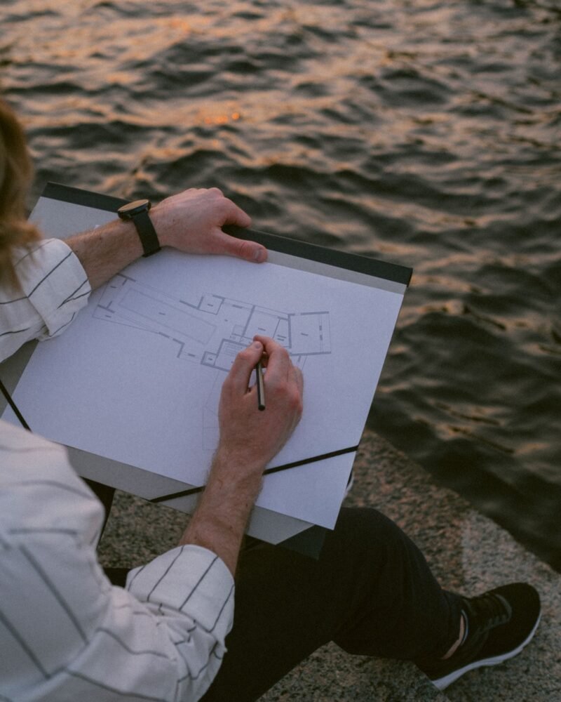 A person sketching a floor plan on a clipboard beside the water