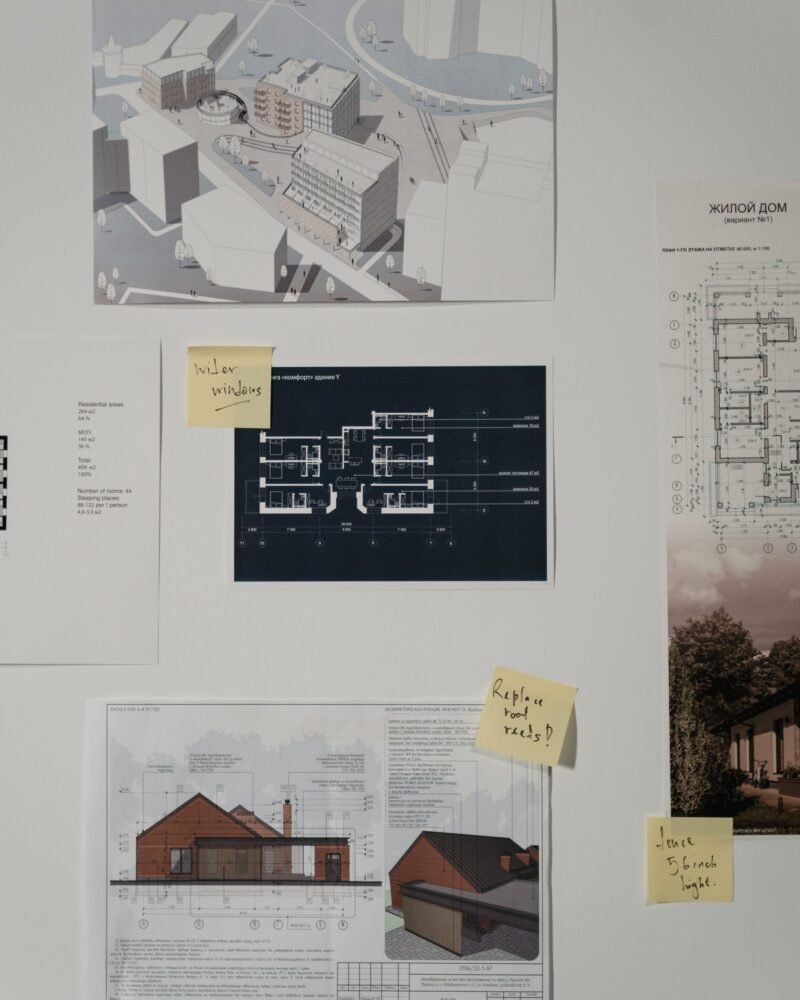 Architectural renderings, floor plans and house elevations pinned to a wall with handwritten sticky-note revisions