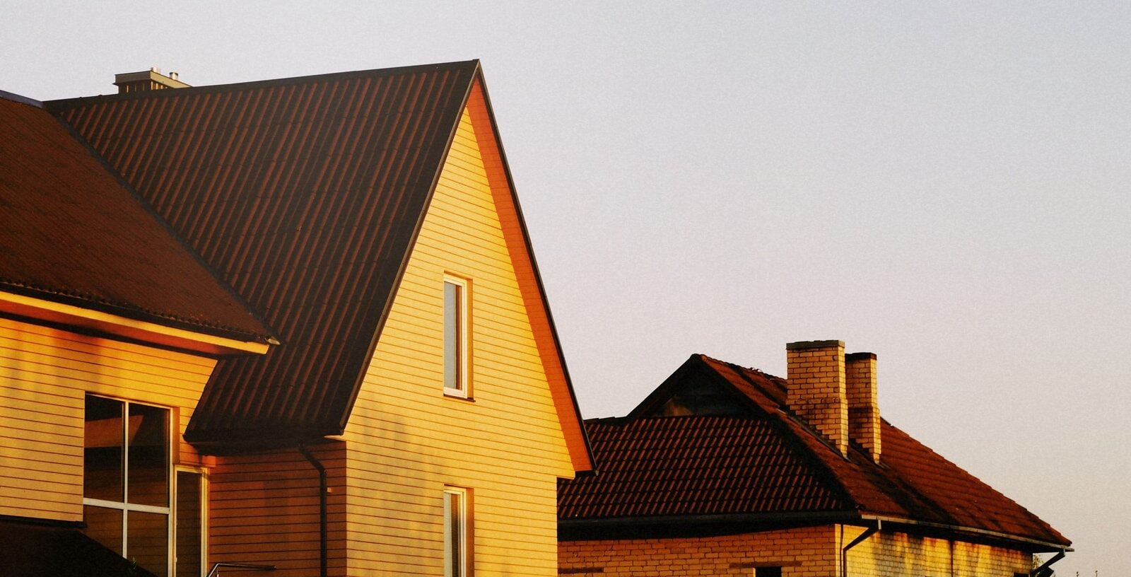 Two pitched-roof suburban houses lit by low golden sun against a pale evening sky