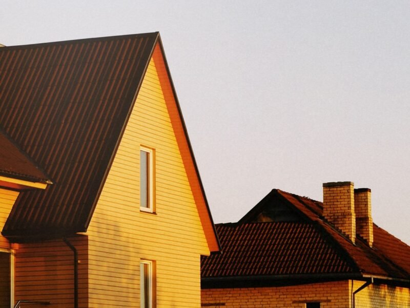 Two pitched-roof suburban houses lit by low golden sun against a pale evening sky