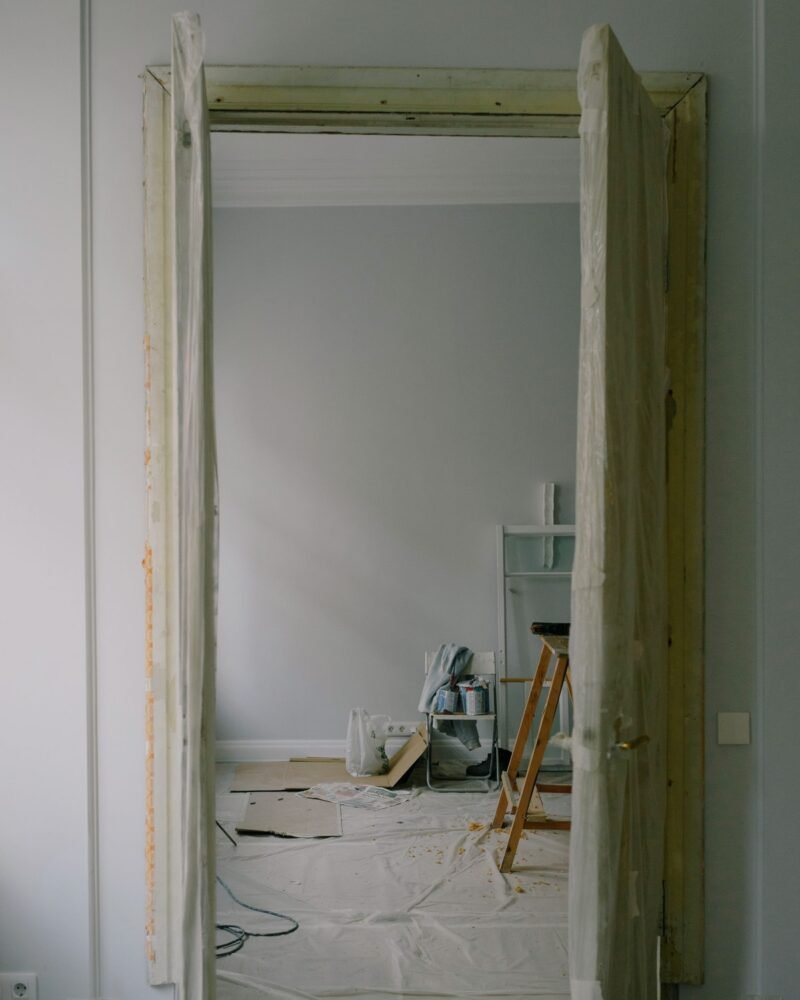 An open doorway into a room under renovation, drop cloths on the floor and a wooden stepladder beyond